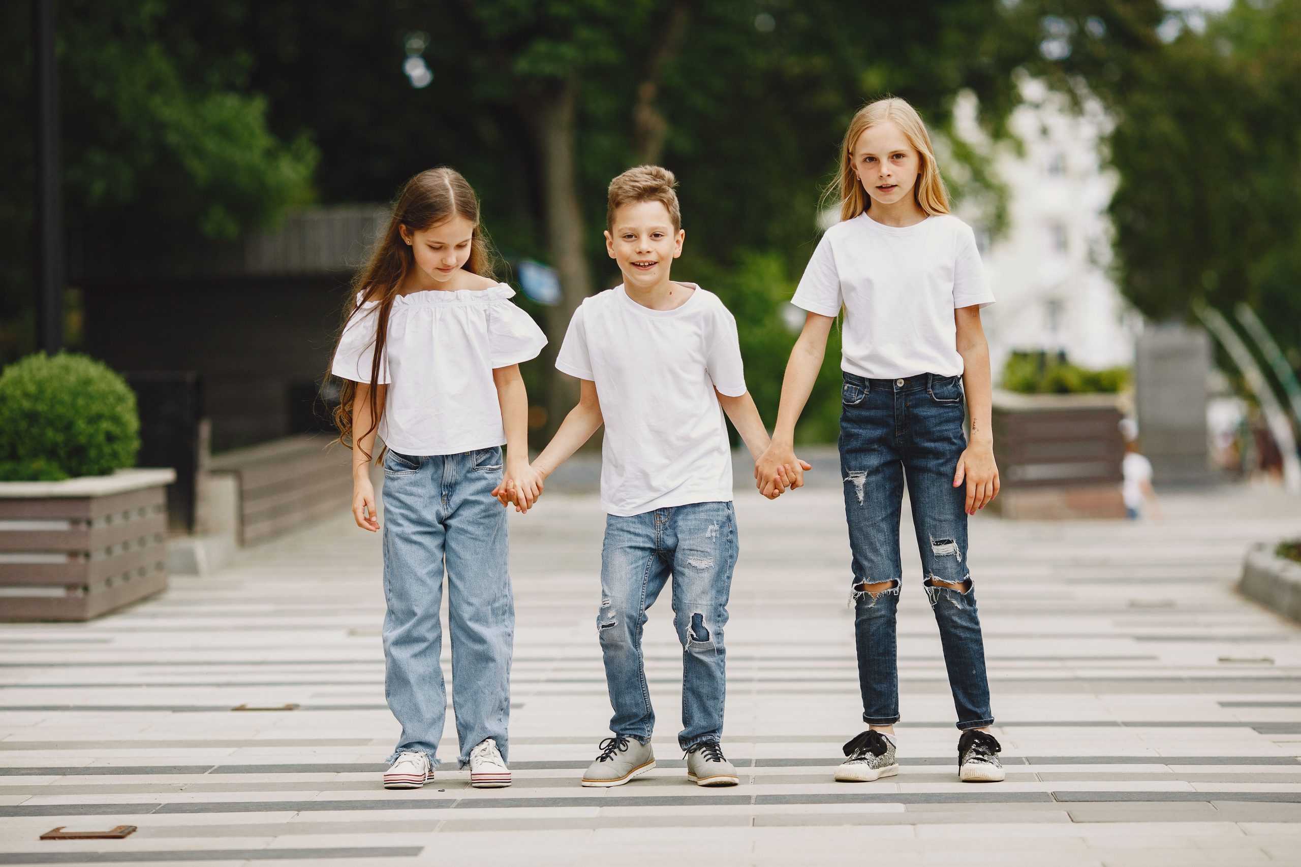 Trois enfants en t-shirts blancs se tenant la main dehors