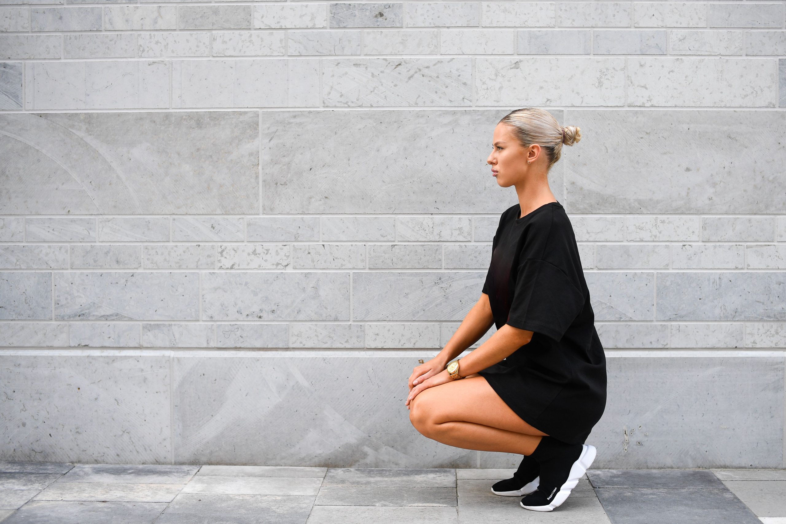 Jeune femme streetwear accroupie contre mur minimaliste